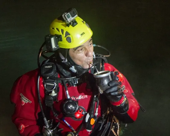 Alfredo Marinaro con equipo de buceo de cuevas, casco y luces, tomando mate