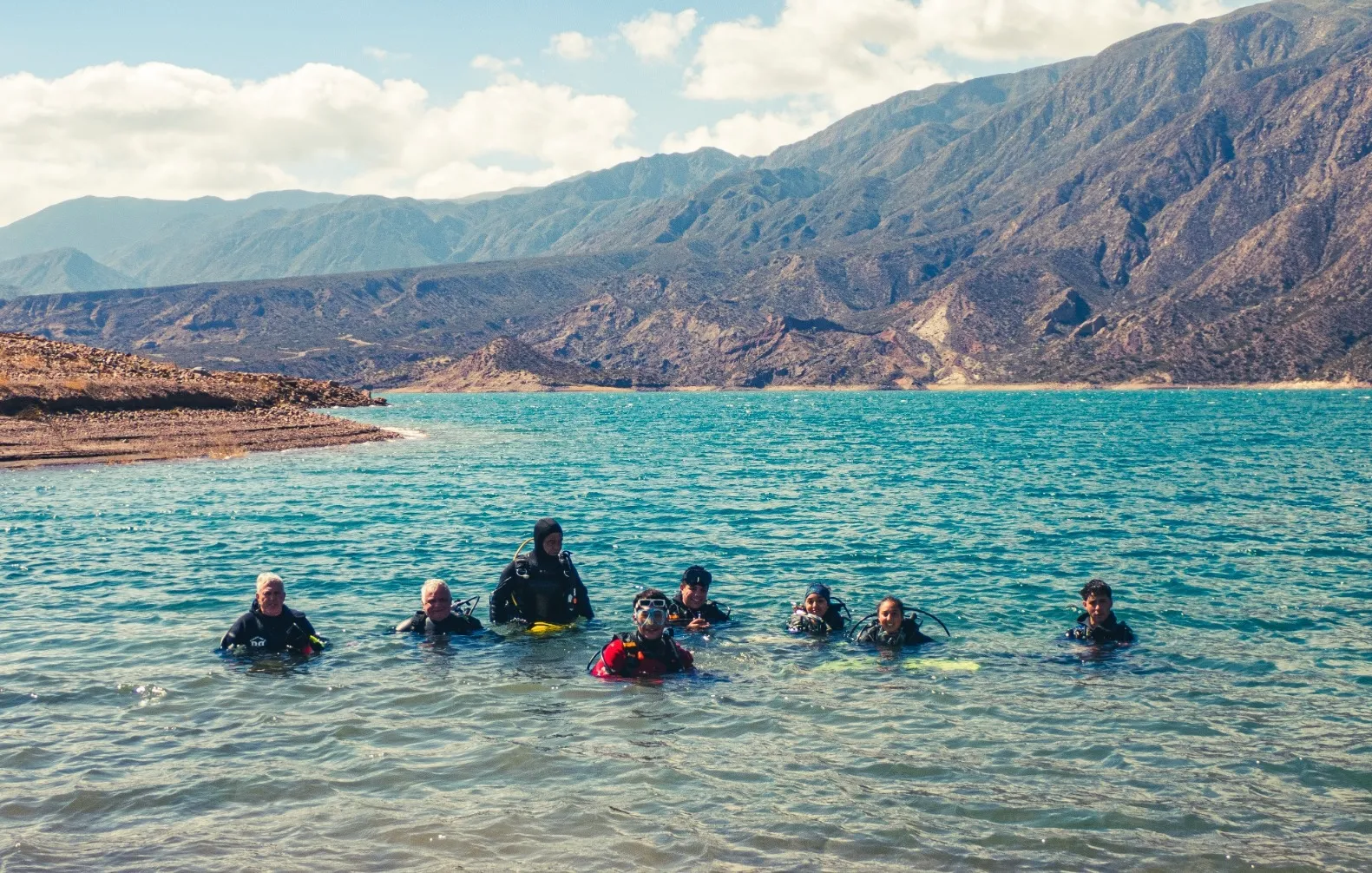 Grupo de buzos en el agua del dique Potrerillos, con la precordillera de fondo