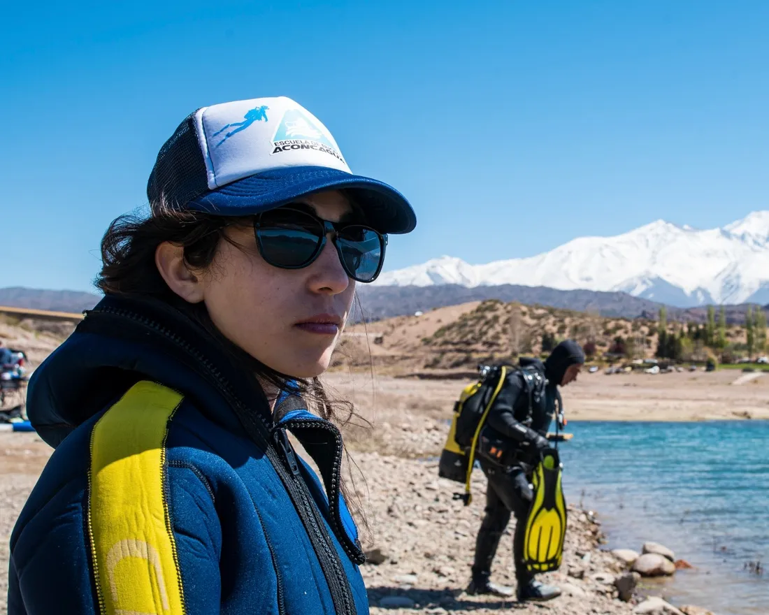 Lucía Marinaro, instructora de buceo de Buceo Aconcagua, a orillas de un dique con la cordillera nevada de fondo